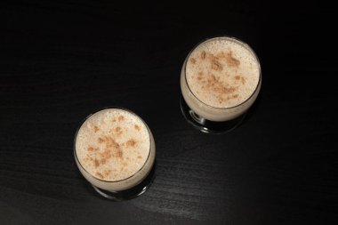 Yakın çekim, üst görüş. Şeffaf bir şarap kadehinde, siyah arka planda rendelenmiş hindistan cevizi serpiştirilmiş eggnog Noel kokteyli..