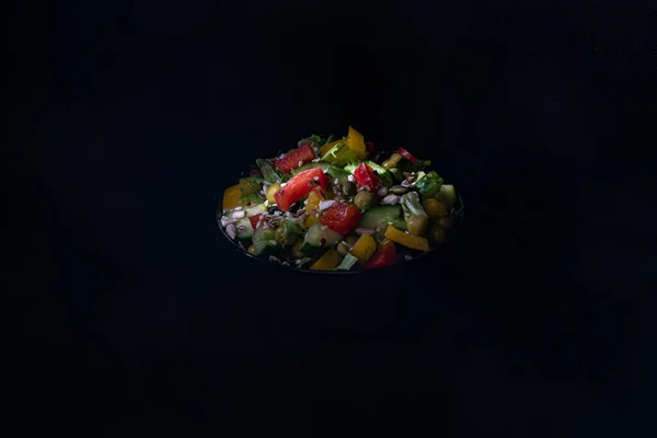 Vegetable salad in a dark bowl on a dark background. Green Leaf Lettuce, cucumber, bell pepper, green peas, black and green olives, sprinkled with sunflower seeds, pumpkin seeds, sesame seeds.