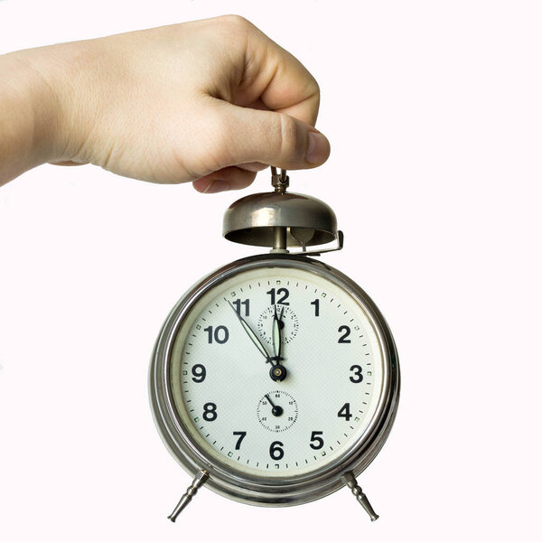 рука держит будильник, показывающий время - от пяти минут до двенадцати - часы лицом
