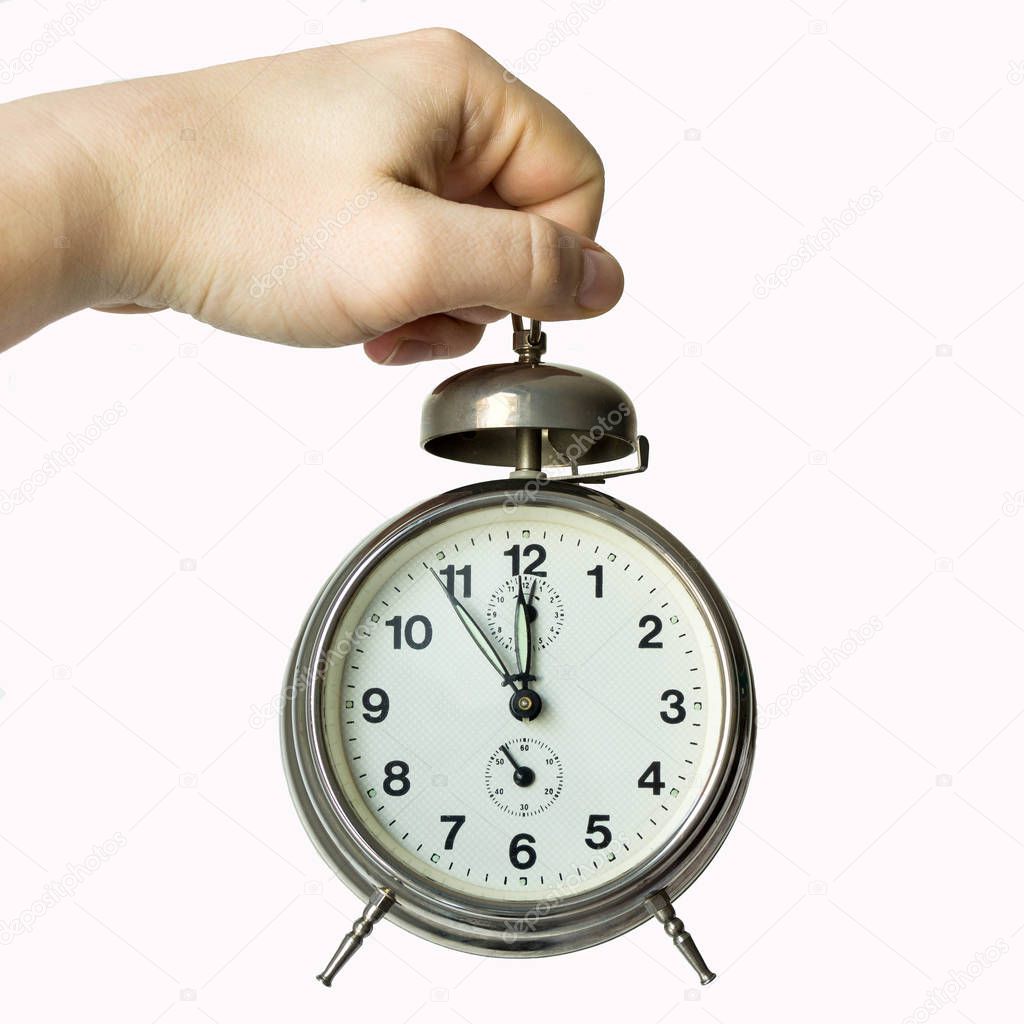hand holding an alarm clock showing the time - five minutes to twelve - clock face
