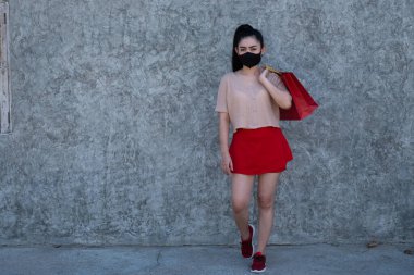 Suratı beton duvarda alışveriş torbaları tutan Asya 'lı güzel bir kadının portresi. Pembe elbiseler ve kameraya bakan kırmızı etek giyen kadınlar.