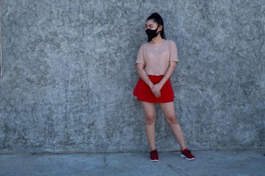 Güzel, genç bir Asyalı kadının portresi. Pembe elbiseler ve kırmızı etek giyiyor. Duvarın arkasında dikiliyor.