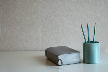 Bir kitap ve pastel kalemler gri arka plandaki masanın üzerindeki mavi bardakta.