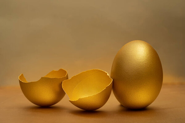 Golden egg and half broken eggs with yolk at the golden background