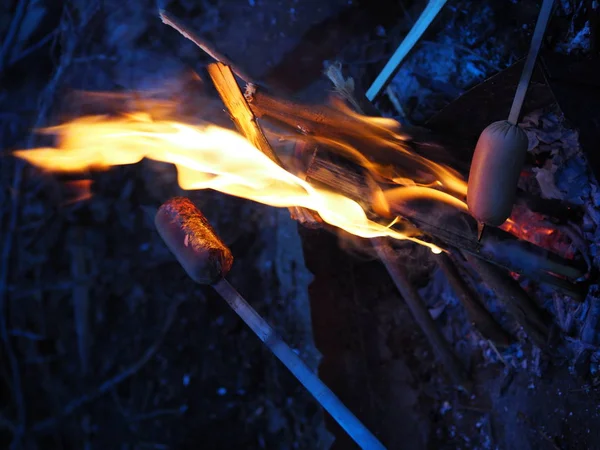 Faire frire les saucisses dans le feu la nuit. Les saucisses au feu et à la flamme sont frites jusqu'à tendreté croquante . — Photo