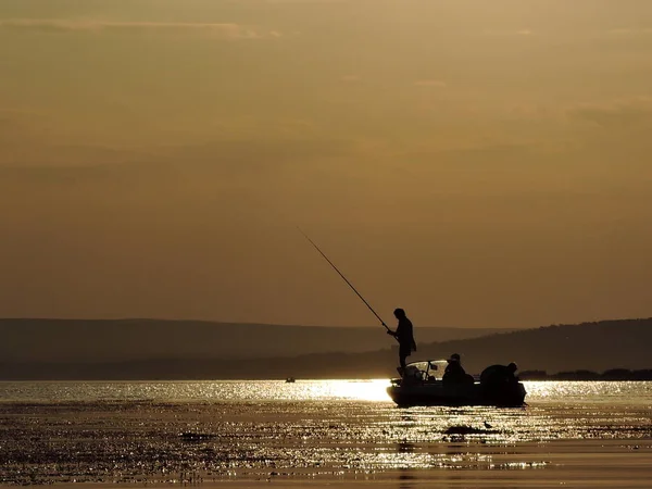 Silhueta de pescadores em um barco com sol amarelo e laranja no fundo — Fotografia de Stock