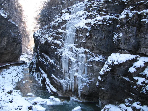 冬の山の川のほとりにつららを張り出した大きな岩 — ストック写真