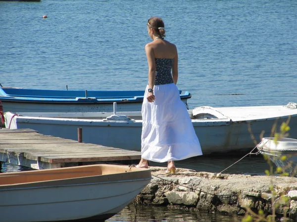 Девушка идет вдоль пляжа в солнечный день. впереди деревянного моста, к которому привязаны лодки . — стоковое фото
