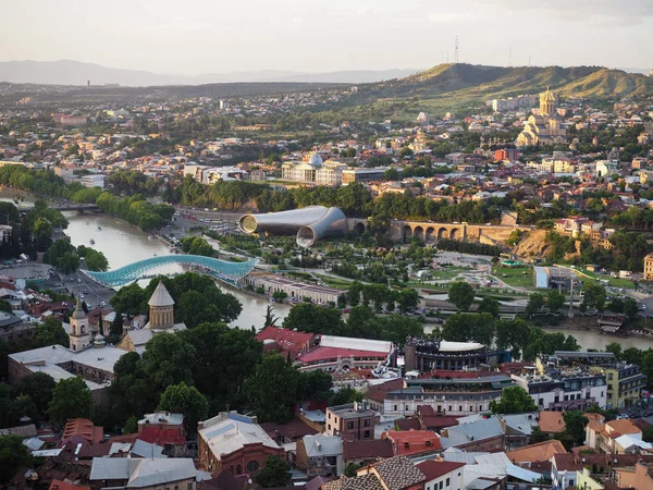 Luftaufnahme von der narikala-Festung auf der georgischen Hauptstadt Tiflis, voller kleiner Ziegeldachhäuser, grüner Bäume, Brücken über den Kura-Fluss — Stockfoto