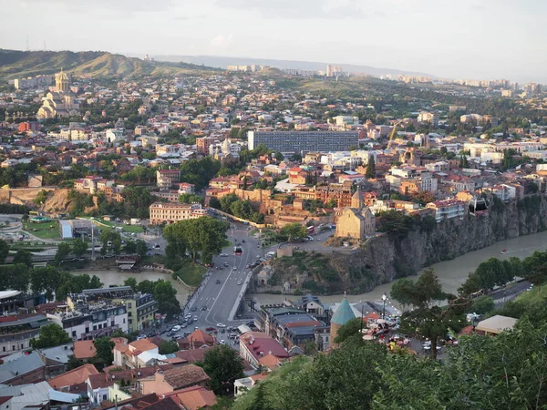 Luftaufnahme von der narikala-Festung auf der georgischen Hauptstadt Tiflis, voller kleiner Ziegeldachhäuser, grüner Bäume, Brücken über den Kura-Fluss — Stockfoto