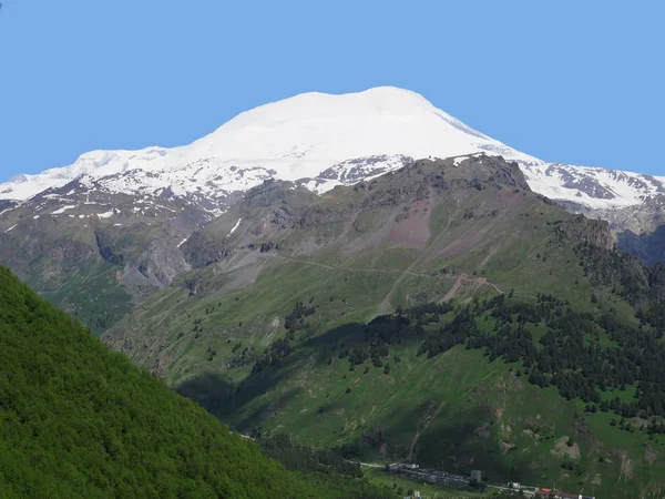Grande catena montuosa natura. Incredibile prospettiva di montagna caucasica neve o vulcano Elbrus con campi verdi, sfondo cielo blu. Elbrus vista paesaggio - la vetta più alta della Russia e dell'Europa — Foto Stock