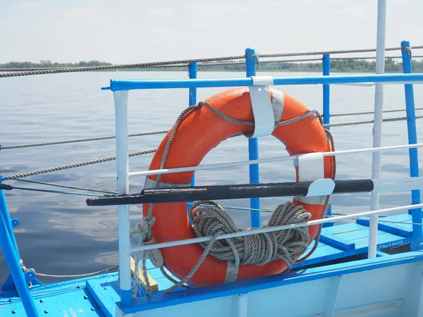 Pomerančová bóje s provazem na dřevěném molu blízko moře. Closeup záchranného Buoy na doku. Záchranné prostředky pro nouzový stav vody Záchranné kruhy na palubě pro záchranu cestujících. — Stock fotografie