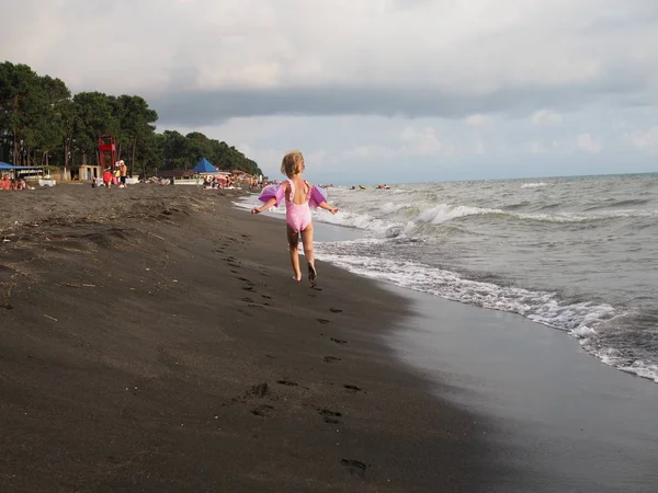 Una niña de tres años corre por la playa contaminada con espuma. georgia, ureki - junio 2019 — Foto de Stock