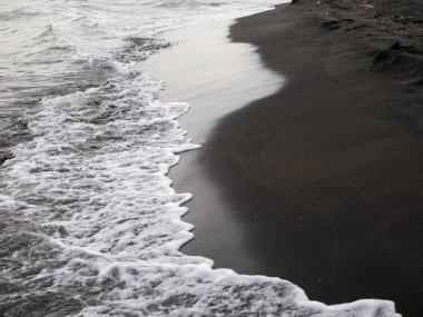 Siyah kumsalda beyaz köpük dalgası.