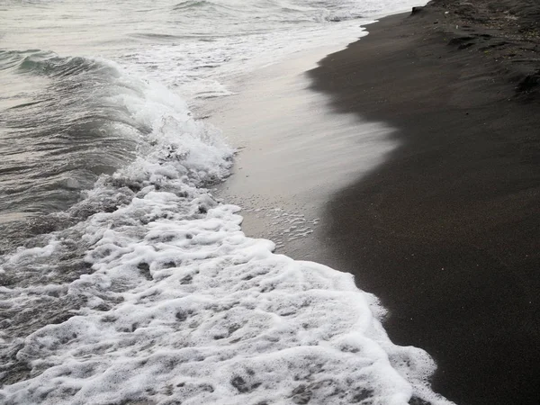 Weiße Schaumwelle am schwarzen Sandstrand. — Stockfoto
