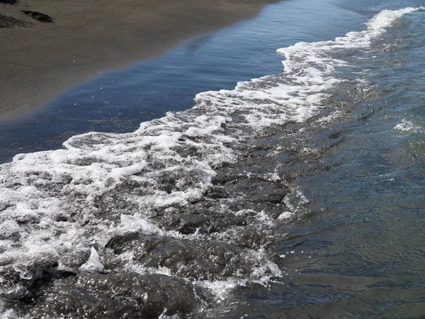 Weiße Schaumwelle am schwarzen Sandstrand. — Stockfoto