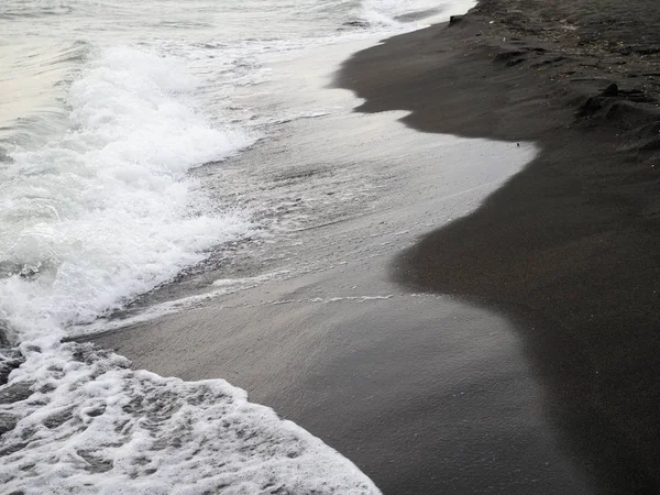 Weiße Schaumwelle am schwarzen Sandstrand. — Stockfoto