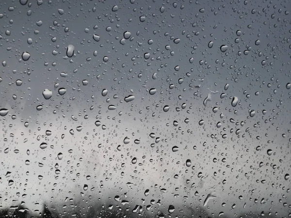 Hermosas gotas de lluvia en el vidrio a través del cual se puede ver el cielo gris tormentoso —  Fotos de Stock