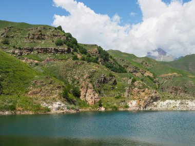 Kayalık dağların tepelerini beyaz bulutlar kaplıyor. berrak dağlı gölün yanında berrak su ve dağlarla Alp çayırları.