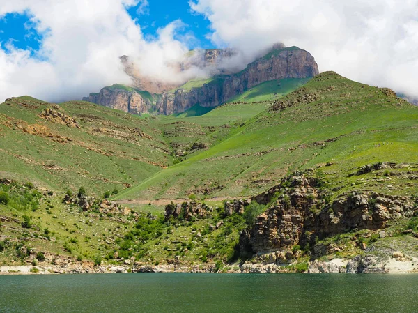 White clouds cover the tops of the rocky mountains. near the pond with clear mountain clear water and mountains with Alpine meadows — Stock Photo, Image