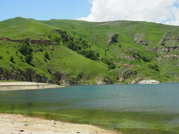 Hermoso paisaje con vistas al lago con agua clara y clara que refleja las montañas cubiertas de hierba verde y visible en la distancia turistas. la gente vino a admirar la belleza natural —  Fotos de Stock