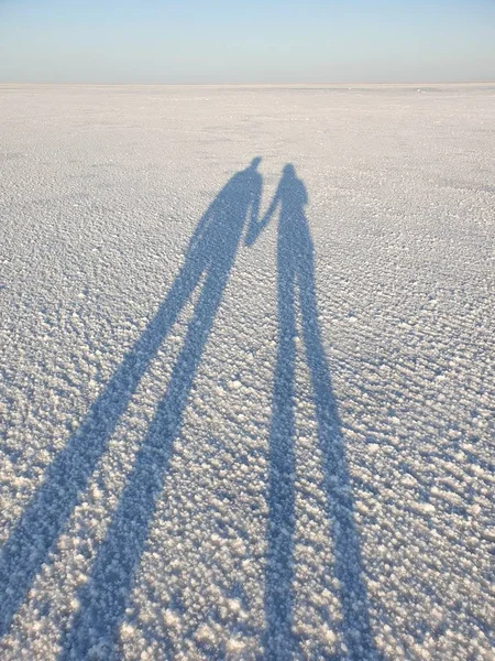 Stín dvou lidí, kteří za úsvitu drží ruce na hladině solného jezera — Stock fotografie