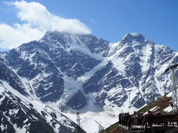 Os turistas se sentam em um café no alto das montanhas e admiram as belas vistas das montanhas. Bela paisagem montanhosa do Cáucaso. Vista da geleira chamada Seven.Russia, Elbrus-June, 2019 — Fotografia de Stock