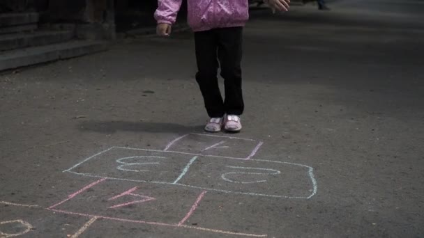 Beine eines kleinen Mädchens, das auf der Straße auf Hopscotch springt. Beine aus nächster Nähe. — Stockvideo