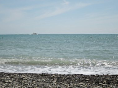 Ufukta deniz yatı, mavi gökyüzü ve bulutlar, ön planda kayalık plaj.