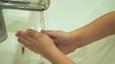 Çocuk ellerini musluğun altında yıkıyor..
