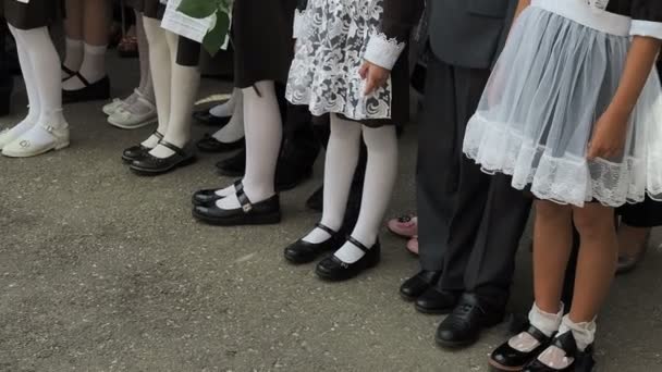 Dziewczyny szkoły podstawowej z bukietami kwiatów w rękach. Buty na jej stopach i białe rajstopy, skarpety i pończochy. Impreza na podwórku szkolnym na początku roku szkolnego. Rosja — Wideo stockowe