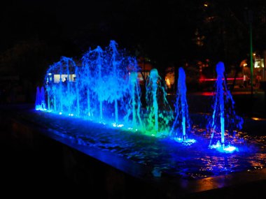 Geceleri yuvarlak ışıklı fıskiyenin bulanık arkaplanı. Geceleri çok renkli dans eden güzel fıskiyeler. Geceleri renkli ışıklarla dolu çeşme.