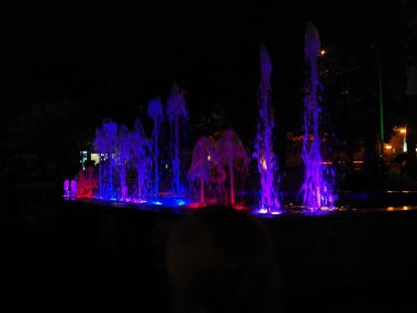 Geceleri yuvarlak ışıklı fıskiyenin bulanık arkaplanı. Geceleri çok renkli dans eden güzel fıskiyeler. Geceleri renkli ışıklarla dolu çeşme.