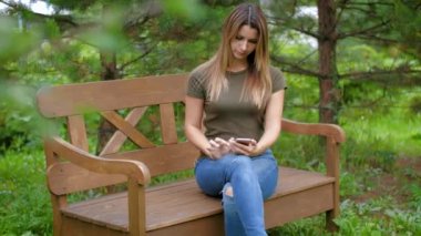 Yalnız bir bankta oturan kadın. Kızın ağaçları arasında bir bankta oturmuş smartphone kullanır. Pitoresk bir yerde bir bankta oturan kadın.