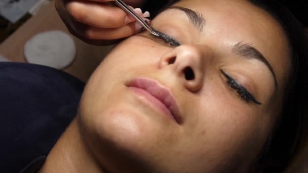 Removal of old lashes. The beautician removes the eyelashes with tweezers. Eyelash extension. Beautiful young woman on eyelash extension procedure. — Stock Video