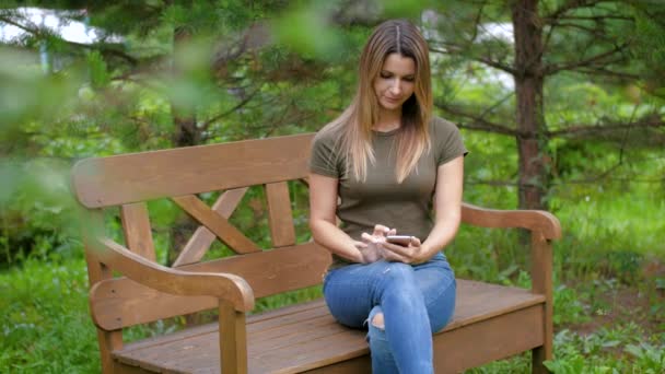 De vrouw zit op een bankje verwijdert de smartphone na aankomst van het kind. Het meisje gaat om haar moeder en gaat zitten op haar knieen. — Stockvideo