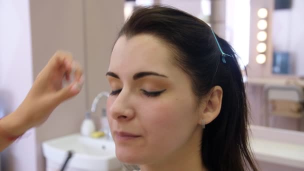 Umělec si na tváři mladé ženy aplikal make-up. Holka dělá v profesionálním salónu make-up. Večerní make-up. Kouřoví oči. 4k — Stock video
