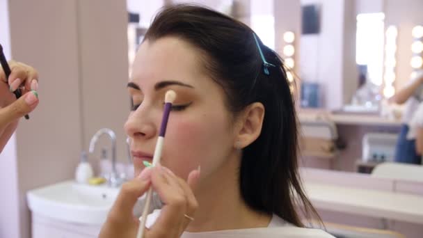 Umělec si na tváři mladé ženy aplikal make-up. Holka dělá v profesionálním salónu make-up. Večerní make-up. Kouřoví oči. 4k — Stock video