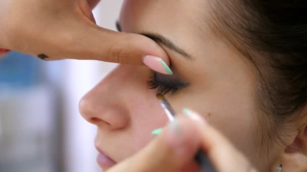 Руки визажиста наносят макияж на лицо молодой женщины. Девушка делает макияж глаз в профессиональном салоне. Вечерний грим. Глаза Смоки. 4k — стоковое видео