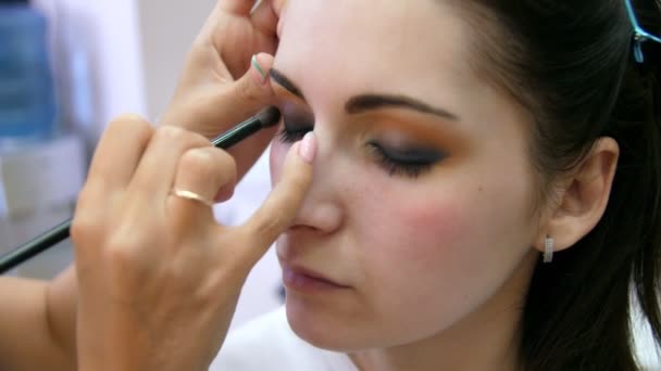 Mains maquilleuse appliqué maquillage sur le visage d'une jeune femme. Fille qui se maquille les yeux dans un salon professionnel. Maquillage de soirée. Yeux fumés. 4k — Video