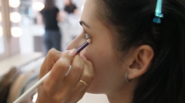 Eller makyaj sanatçısı genç bir kadının yüzüne makyaj uyguladı. Profesyonel bir salonda göz makyajı yapan kız. Akşam makyajı. Dumanlı gözler. 4k