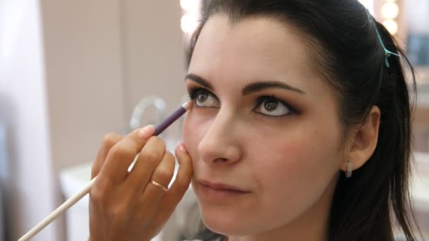 Manos maquillador aplicado maquillaje en la cara de una mujer joven. Chica haciendo maquillaje de ojos en un salón profesional. Maquillaje de noche. Ojos humeantes. 4k — Vídeos de Stock