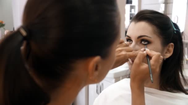 Händer make-up artist appliceras makeup på ansiktet av en ung kvinna. Flicka gör ögonmakeup i en professionell salong. Kvällsmakeup. Smokey ögon. 4K — Stockvideo