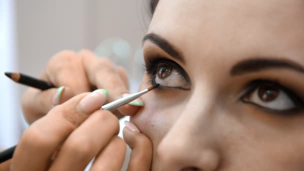 Manos maquillador aplicado maquillaje en la cara de una mujer joven. Chica haciendo maquillaje de ojos en un salón profesional. Maquillaje de noche. Ojos humeantes. 4k — Vídeo de stock