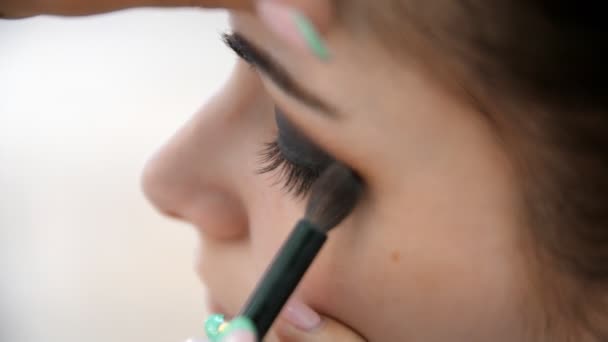 Manos maquillador aplicado maquillaje en la cara de una mujer joven. Chica haciendo maquillaje de ojos en un salón profesional. Maquillaje de noche. Ojos humeantes. 4k — Vídeo de stock