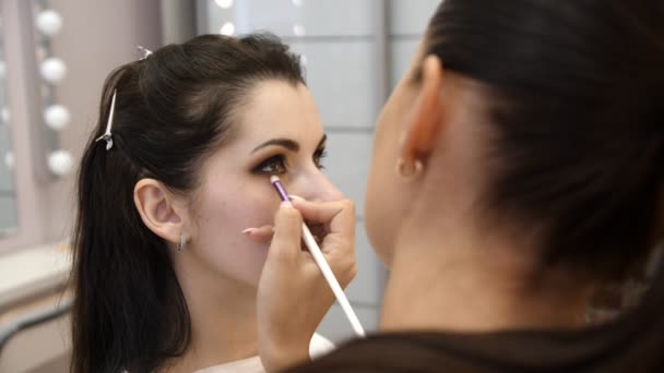 Manos maquillador aplicado maquillaje en la cara de una mujer joven. Chica haciendo maquillaje de ojos en un salón profesional. Maquillaje de noche. Ojos humeantes. 4k — Vídeo de stock