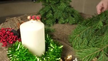 Kadın elleri Noel kompozisyon için köknar dalları hazırlamak. Masaya yatıp ellerini koparıyorlar. Bir Noel kompozisyonu oluşturuyor. Soldan sağa kamera hareketi, yakın.