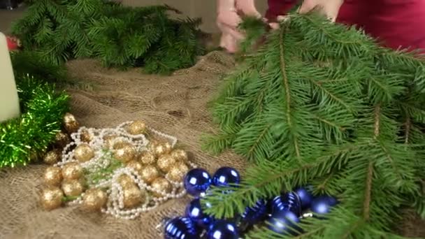 Fiorista prepara rami di abete per la composizione di Capodanno sullo sfondo di giocattoli di Natale lucido. Creare una composizione natalizia. Da vicino. . — Video Stock
