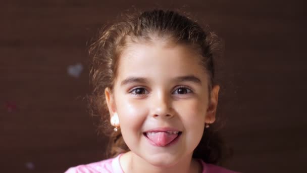Portré egy fogatlan mosolyú kislányról. A gyerek a fogai között lévő lyukon keresztül mutatja a nyelvét. Hogy megmutassuk a fogak hiányát. — Stock videók