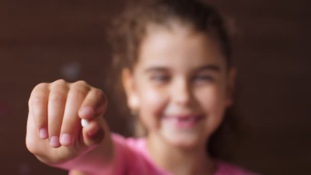 Retrato de una niña con una sonrisa sin dientes. Muestra un diente rasgado en la cámara con una mano extendida. Cambia el enfoque de diente a cara. Ríe en voz alta . — Vídeos de Stock